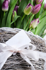 Close-up of purple tulips in rustic wicker basket with blank gift tag and white ribbon, floral gift concept