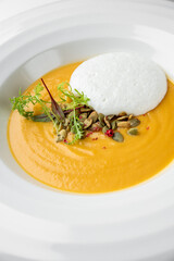 Gourmet pumpkin soup served in a white bowl, garnished with seeds, microgreens, and a crisp cracker. Minimalist fine dining presentation on a restaurant table.