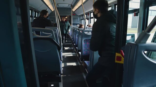 Man boarding a city bus with several seated passengers and empty seats interior view of public transport person wearing a coat and mask entering the bus urban commuting scene daytime travel - Powered by Adobe