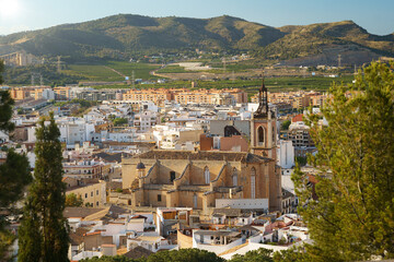 Historic Sagunto church cityscape. An elevated view of Santa Maria Cathedral nestled among rooftops with rolling hills in the background, great for Spanish travel media.