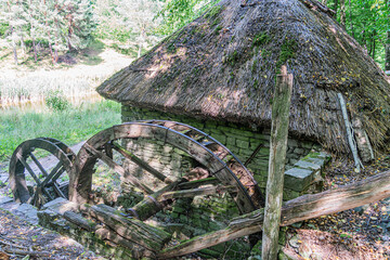 Tranquil, old water wheel in a Central European village, rustic wooden structure, signs of age and wear, thatched roof, moss patches, lush greenery, soft lighting, solitude, abandonment, elevated per