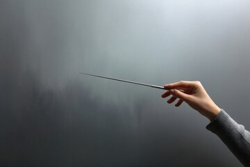 A hand holding a pointer against a gray background, symbolizing teaching, leadership, and guidance.