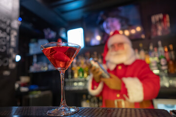 Santa Claus works at the bar making cocktails in a shaker. 