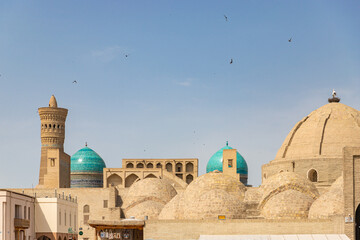 Awesome view of roof of the Trading Dome Toqi Zargaron and dome of the Mir-i-Arab Madrasa in Bukhara, Uzbekistan. The Kalan Minaret of Po-i-Kalan complex is visible on blue sky background