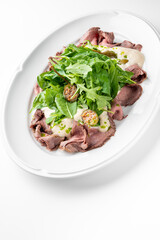 Gourmet roast beef salad with arugula, spinach, capers, and creamy dressing on a white plate. Minimalist presentation, fresh ingredients, restaurant-style plating.