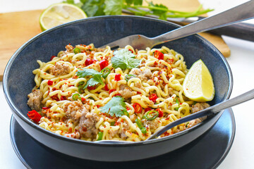 Spicy noodles with chillies, coriander and lemon with fork and spoon in a bowl.
