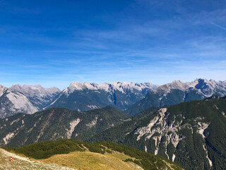 Majest&auml;tische Alpenlandschaft mit klarer Fernsicht, gr&uuml;nen Bergw&auml;ldern und schroffen Felsgipfeln unter tiefblauem Himmel &ndash; typisches Panorama der Tiroler Alpen an einem sonnigen Sommertag.