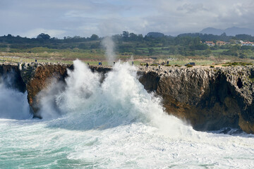 Visitors and tourists walk above the cliffs of Pria with waves crashing against the rocks