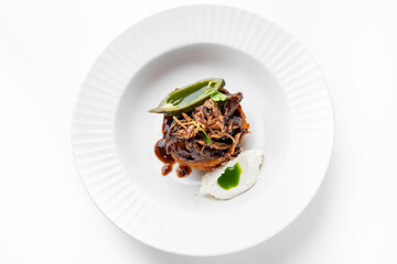 Gourmet beef dish with crispy base, rich sauce, fried onions, herbs, and creamy side, plated on white fluted plate. Elegant restaurant-style presentation, top view.