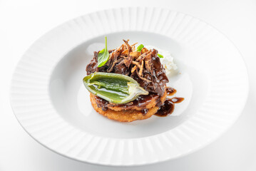 Gourmet beef dish with crispy base, rich sauce, fried onions, herbs, and creamy side, plated on white fluted plate. Elegant restaurant-style presentation, top view.