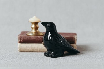 Black Bird Figure Next to Candle and Vintage Books on Gray Background
