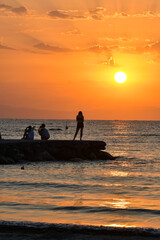 Paralia, Katerini, Greece, 14.08.2025: Sunrise over the sea in Paralia, Katerini, Greece. Silhouettes of people and a girl standing against the sun.