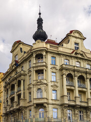 Fototapeta premium Detailed close-up of an elegant classical building facade featuring ornate stone carvings sculptures and a dark dome-shaped tower under a soft grey sky.