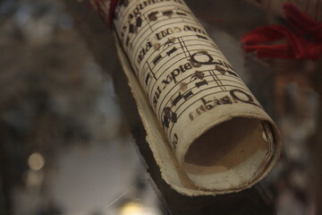 Close-up of a rolled scroll of antique, aged musical notation (sheet music) on parchment-like paper, featuring medieval or Gregorian chant style script and notes, tied with red string.