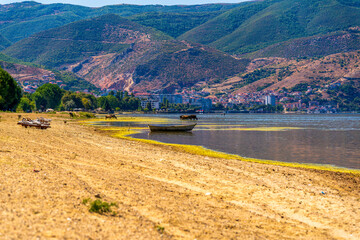 Naklejka premium Scenic view of Lake Ohrid near Pogradec, Albania with calm water, distant mountains, and a wooden boat under bright summer sunlight