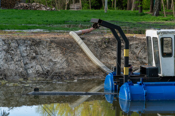 Industrial dredging machinery floating on a small body of water near an exposed earthen slope with green foliage