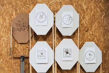 Various paper shooting targets attached to backboards on a wooden OSB wall, showing clustered...