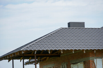 Fototapeta premium Unfinished residential building exterior with a newly installed dark grey metal roof and visible wooden rafters