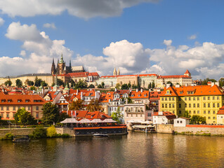 Obraz premium Beautiful landscape of a historical riverside city area with vibrant yellow buildings and red roofs reflecting in the river water under a bright sky with large white cumulus clouds.