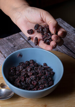 Manipulacion de alimentos, manejo de comida en la cocina, Mano femenina vaciando pasas dentro de un  tazon azul sobre una tabla de cortar en una mesa rustica de madera con fondo oscuro