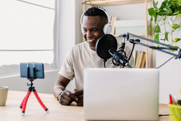 Young man wearing headphones and using a microphone, recording online video or audio content with smartphone and laptop