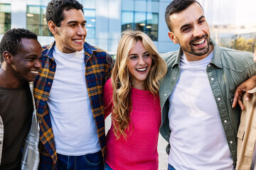 Group of cheerful multiracial friends embracing while laughing at city street. Friendship, youth,...