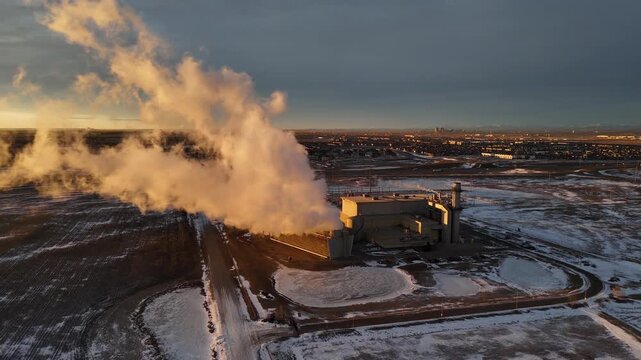 Sunrise rotating aerial steam rising of gas fire power plant overlooking distant city in Alberta Canada.
