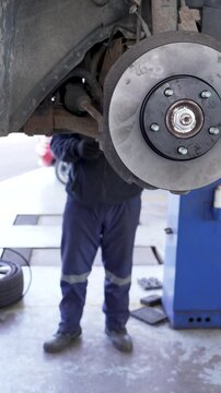 Close-up of a vehicle's brake disc and caliper with a mechanic working in the background