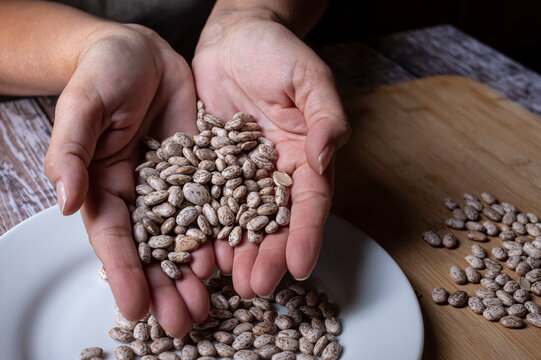 Manipulacion de alimentos, manejo de comida en la cocina, manos femeninas tomando frijoles pintos colocandolos en un plato blanco de ceramica sobre una mesa de madera con un fondo oscuro
