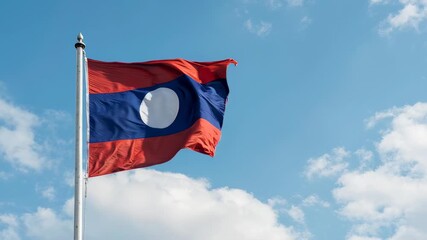 The national flag of Laos waving in the wind against a bright blue sky with scattered white clouds.