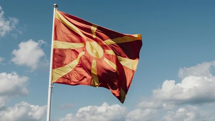 The flag of North Macedonia waving in the wind against a bright blue sky with scattered white clouds.