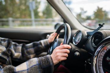 Closeup of woman hands holding steering wheel driving modern vehicle. Female traveling by car, observing speed limit, drives through the countryside, with autumn landscape visible outside the window.