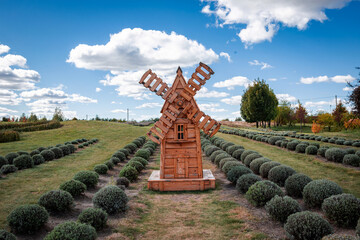 Beautiful wooden vintage windmills stand in a field of blooming flowers against a cloudy sky. Rural romantic landscape with cloudy clear sky.