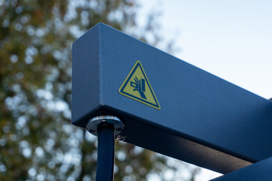 Industrial warning sign on heavy grey metal equipment indicating hand crush hazard outdoors