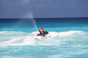 Person riding a jet ski across turquoise ocean waves under a sunny sky, creating a splash of water....