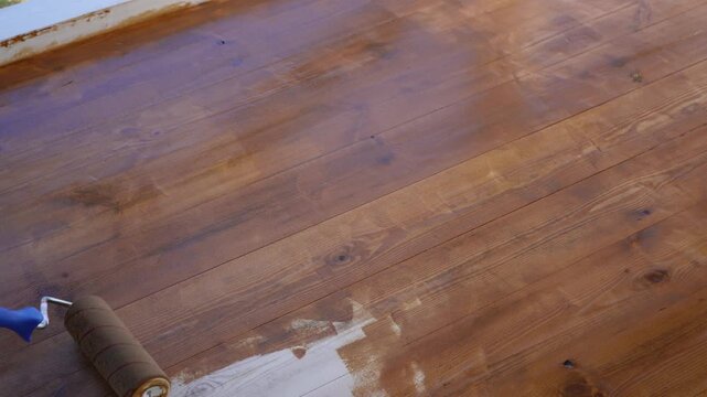 Applying protective wooden deck, yacht varnish , stain using paint roller for a smooth finish