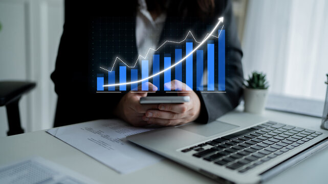 A business professional engaged in financial analysis using a smartphone while examining a digital growth graph overlay in a modern office setting. Impute - Powered by Adobe