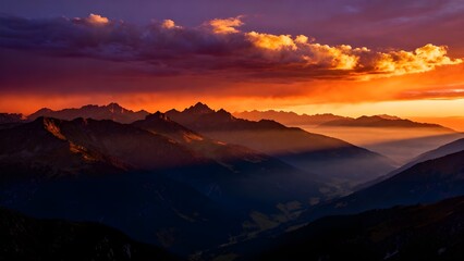 A majestic sunset casts a fiery, golden glow over a layered mountain range. Dramatic clouds fill the vibrant sky as rays of light beam down into the hazy valley below.