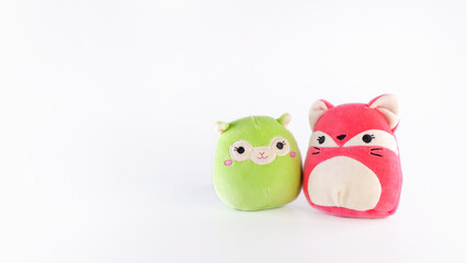 Colorful plush toys featuring a green animal and a pink fox, designed for children, showcasing soft textures and playful expressions in a bright setting