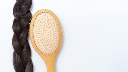 Long dark braided hair next to a wooden hairbrush on a clean white background, showcasing hair...
