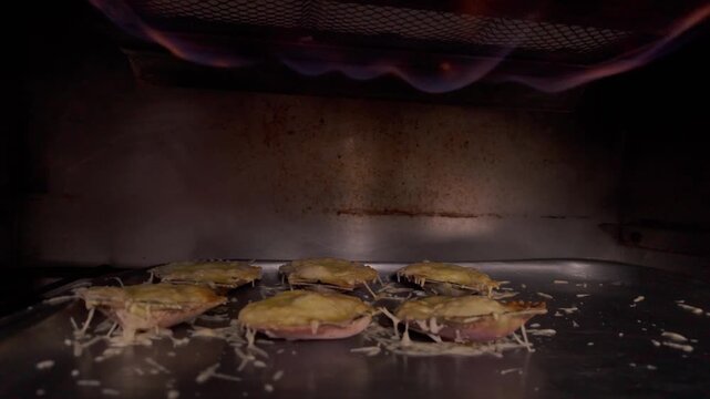 Scallops with parmesan cheese gratinating in a salamander broiler