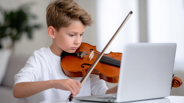 Young boy playing violin while learning online, focused on laptop screen, showcasing dedication to music education and skill development in a bright, modern environment