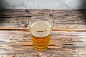 A clear glass filled with golden yellow drink sits atop a rustic wooden table. Bubbles rise to the surface, reflecting light in a cozy setting