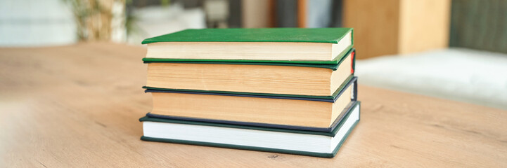 Stack of four hardcover books on wooden table in bright room.
