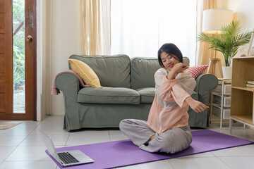 Fototapeta premium Healthy lifestyle woman exercises yoga for physical health, teen workout at home with sport, young Asian woman stretches arm on purple mat watching online fitness on laptop in bright room