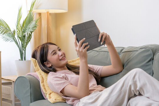 Teen person using tablet, woman relaxing reading digital content, enjoying entertainment, modern communication, happy teen girl smiling at device screen, leisure activity at home sofa
