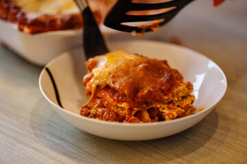Serving delicious lasagna with melted cheese in a white bowl for dinner