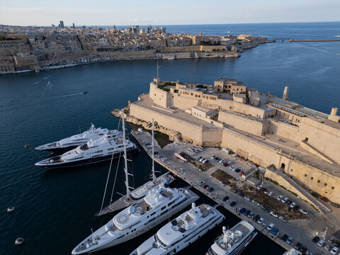 Aerial panorama of luxury superyachts moored at Fort St. Angelo. Historic fortifications and Valletta cityscape in the Grand Harbour, Malta.