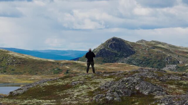 Epic Drone Ascending Shot Revealing a Breathtaking Vist of a Hiker on a Mountain Plateau Overlooking a Vast Lake and Rugged Highland Landscape