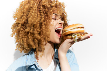 Young woman with curly hair joyfully holding a burger, expressive emotion, bright colors, healthy...
